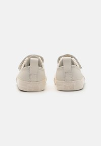 Kremefargede kanvas sneakers med lav toppdesign, som har en teksturert overflate, hvit gummisåle og preget "Converse All Star" merke.