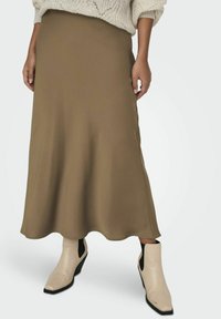 Jupe midi en vert olive, tissu lisse, ourlet légèrement évasé, associée à des bottines crèmes avec des panneaux latéraux noirs et un talon compensé.