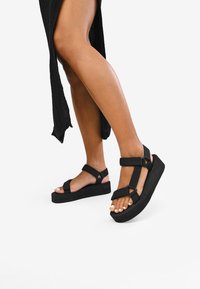 Sandali platform neri con ampie cinghie, tessuto strutturato e suola spessa. Le cinghie sono regolabili per una vestibilità sicura.