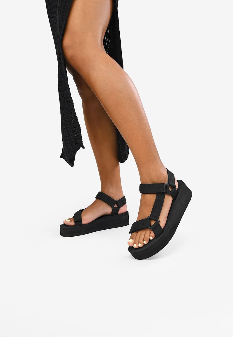 Sandali platform neri con ampie cinghie, tessuto strutturato e suola spessa. Le cinghie sono regolabili per una vestibilità sicura.