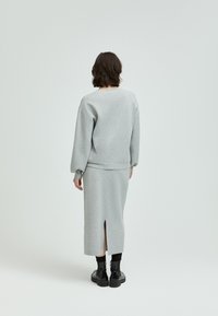 Grauer Sweatshirt mit langen Ärmeln, kombiniert mit einem passenden grauen Rock mit einem Schlitz auf der Rückseite; das Modell trägt schwarze Stiefel. Glatte Textur insgesamt.