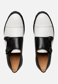 Schwarz-weiße Leder Schuhe mit Schnallenverschluss, runder Zehenform, strukturierten schwarzen Akzenten und einer stabilen, flachen Sohle.