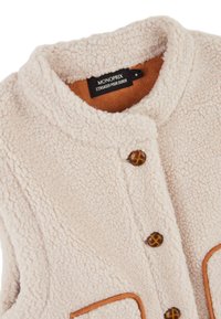 Gilet en polaire beige avec un col rond, des bordures marron et deux poches frontales. Comprend trois fermetures à boutons marron avec un design texturé.