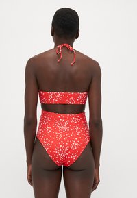 Rode bikini set met een hooggetailleerde broek, halternek top en een wit bloemmotief. Soepele stof met een verstelbare strik bij de nek.
