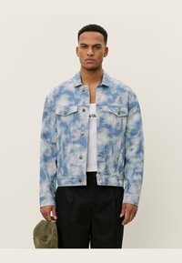 Light blue denim jacket with a cloud pattern, button closure, two chest pockets, and a structured design. Worn over a white shirt.