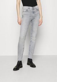 Jeans ajustados grises de mezclilla, con bolsillos frontales, una cintura de altura media y costuras laterales. Llevados con botas negras hasta el tobillo.