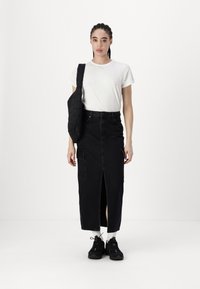 Svart denim maxi skjørt med frontsplitt og sidelommer, kombinert med en hvit bomulls t-skjorte og svarte joggesko, sammen med en quiltet svart skulderveske.