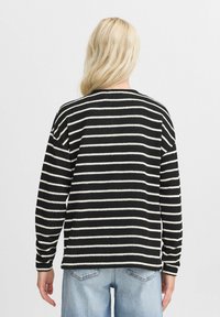 Gestreiftes Schwarz-Weiß-Langarmpullover mit Rundhalsausschnitt und strukturiertem Stoff, kombiniert mit hellblauen Jeans.