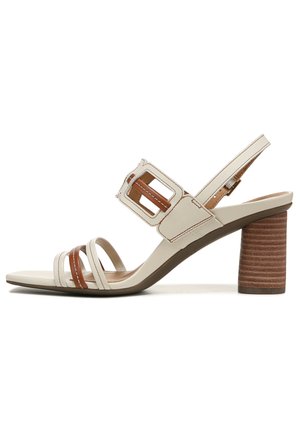 Beige sandal with brown accents, featuring an ankle strap and a chunky, ribbed heel. Strappy design with a square buckle detail.