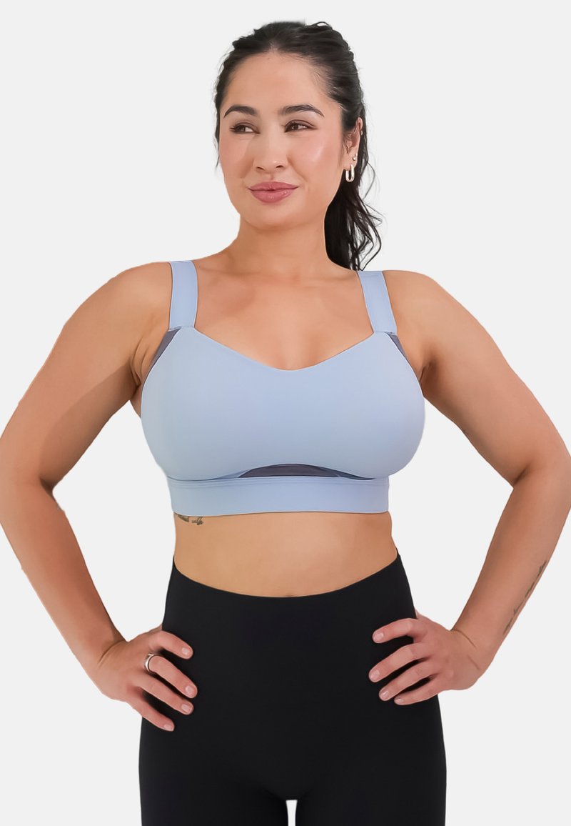Light blue sports bra with a round neckline, wide straps, and mesh detailing. Smooth texture with a fitted design, paired with black leggings.