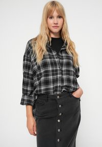 Black and gray plaid button-up shirt with long sleeves, paired with a black denim skirt featuring front buttons and side pockets.