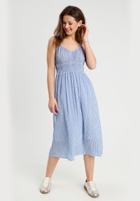 Robe midi à rayures bleu clair avec des bretelles spaghetti réglables, taille smockée et jupe fluide, associée à des baskets argentées.