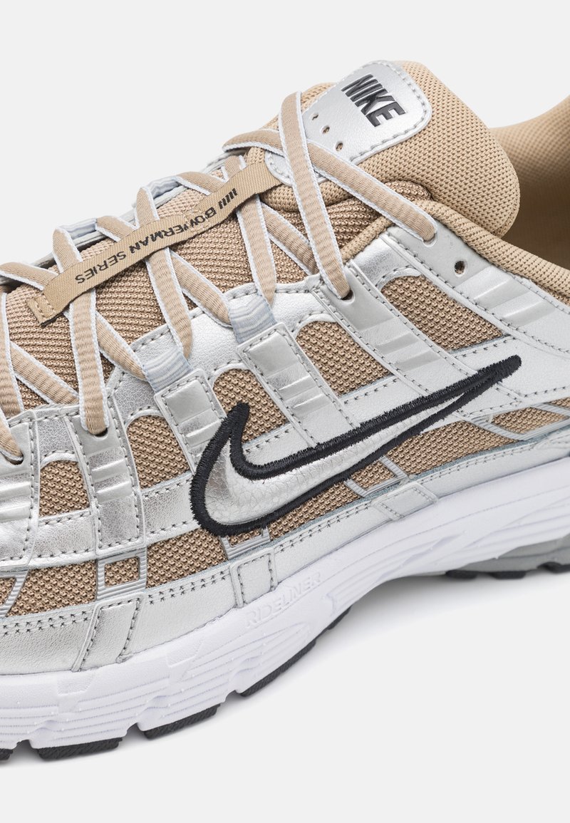 Sneakers Nike z siateczkową cholewką i srebrną skórą, beżowymi akcentami, czarnym logo Swoosh oraz teksturowaną gumową podeszwą.