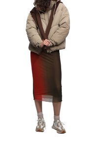 Chaqueta acolchada en beige con detalles marrones, combinada con una falda de malla transparente en varios tonos. Zapatillas blancas y beige, calcetas grises, y ajuste relajado.