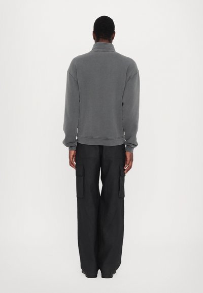 Sudadera de polar gris con cuello alto, hombros caídos y puños acanalados, combinada con pantalones cargo negros de corte suelto que presentan bolsillos laterales.