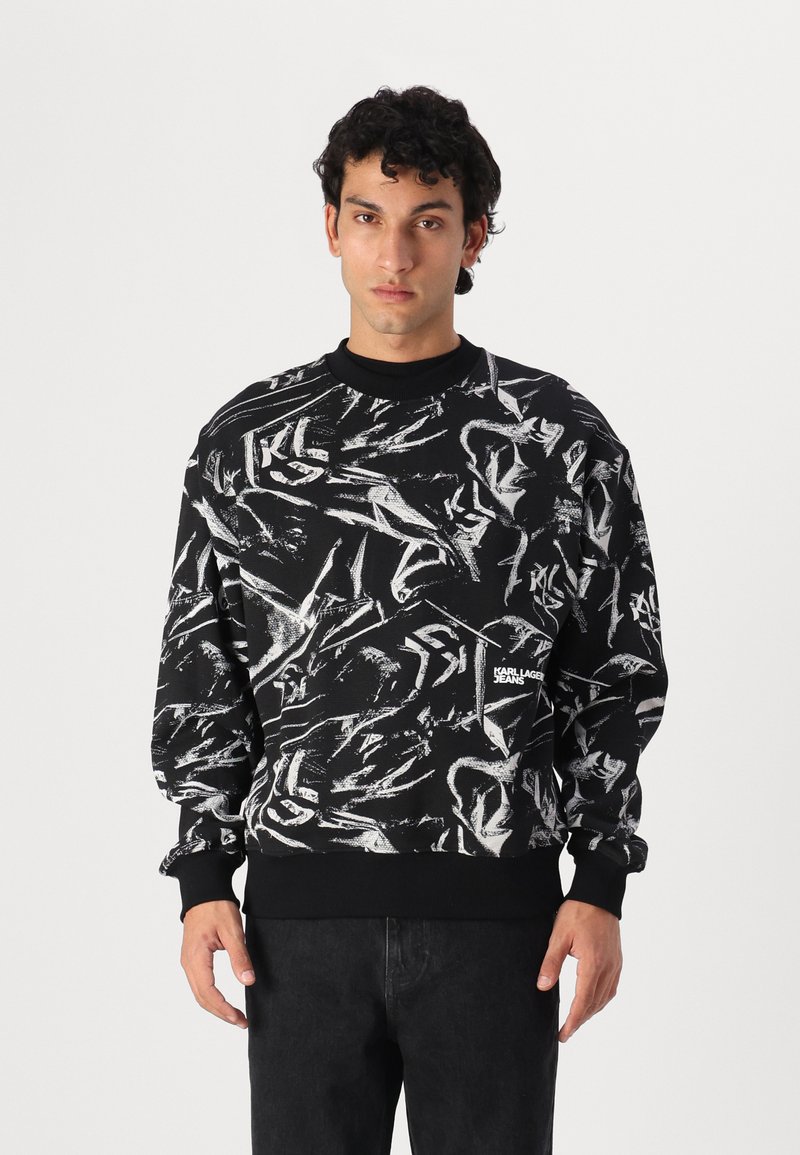 Black sweatshirt featuring abstract white graphic patterns, round neckline, ribbed cuffs, and a logo on the front. Material appears soft.