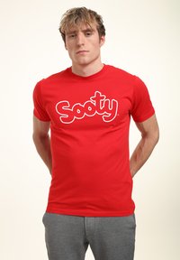 Červené bavlněné tričko s velkým bílým logem "Sooty" na hrudi, kulatým výstřihem a krátkými rukávy. Ležérní střih.