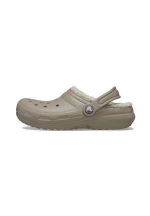 Zueco beige claro con un acabado texturizado, forro de felpa y agujeros de ventilación. Presenta una correa en el talón ajustable y un acento de logo redondo.