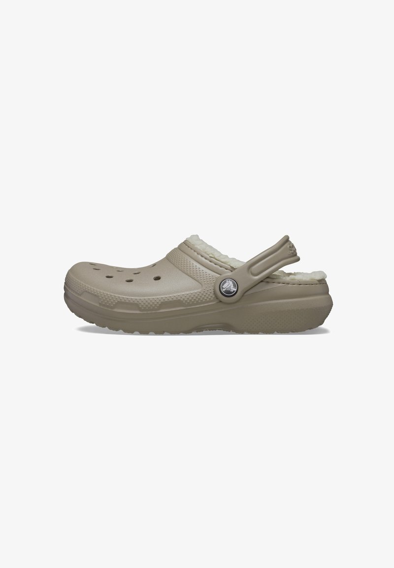 Light beige clog with a textured finish, fuzzy lining, and ventilation holes. Features an adjustable heel strap and a round logo accent.