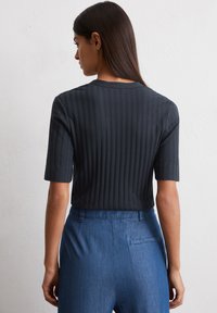 Czarny prążkowany top z krótkim rękawem i okrągłym dekoltem, w połączeniu z niebieskimi spodniami w luźnym kroju z detalem tylniej kieszeni.