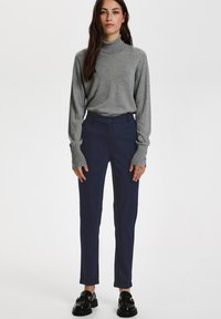 Pelēks augstā kakla džemperis no mīkstas auduma, saskaņots ar tumši ziliem pieguļošiem biksēm ar priekšējo pogu aizdari un sarullētām piedurknēm. Melni mokasīni.