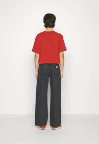 Red short-sleeve t-shirt paired with black wide-leg jeans. The outfit features a relaxed fit and subtle logo patch on the back pocket.