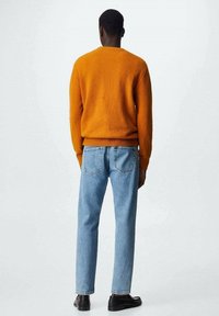 Pull en tricot orange, jean bleu clair et chaussures noires. Le pull a un col rond et un ourlet côtelé ; le jean est droit avec des poches arrière.