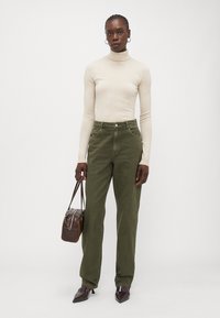 Bežs turtlenecks džemperis, olīvu zaļa plaša kāju korduroja bikses, brūna soma un smaili tumši brūni zābaki. Minimālisma dizains ar klasiskām krāsām.