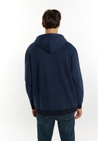 Felpa blu navy con un grande cappuccio regolabile, silhouette allungata, polsini e orlo a coste; tessuto morbido con texture minima e senza motivi.