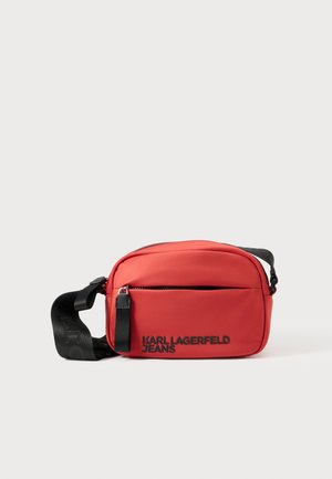 Rdeča najlonska torbica čez ramo z žepom z zadrgo spredaj, nastavljivim trakom in črnim logotipom "KARL LAGERFELD JEANS." Gladek material, kompaktna oblika.