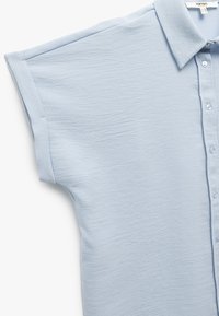 Camicia azzurra a maniche corte realizzata in tessuto testurizzato, con colletto e una fila di bottoni sul davanti. Tessuto morbido e liscio.