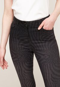 Svarta jeans med ett tonalt zebramönster, med knappstängning och framfickor. Tyget ser slätt och något stretchigt ut.