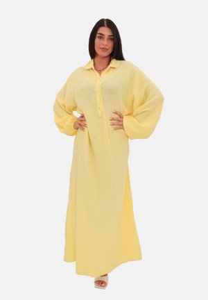 Robe maxi jaune à boutons, confectionnée dans un tissu texturé, avec de longues manches volumiques et une coupe décontractée.