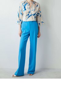 Blusa con colletto a cravatta in crema con motivi astratti blu, abbinata a pantaloni blu a vita alta, con vestibilità sartoriale e gamba larga.