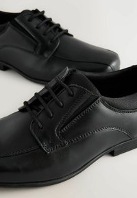 Zapatos de cuero negro con un acabado suave, que presentan un diseño clásico con cordones, detalles de costura sutiles y una forma de punta ligeramente redondeada.