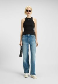 Top senza maniche nero, jeans a gamba larga blu chiaro, sneaker platee bianche e una piccola borsa nera. Tessuto morbido e vestibilità casual.