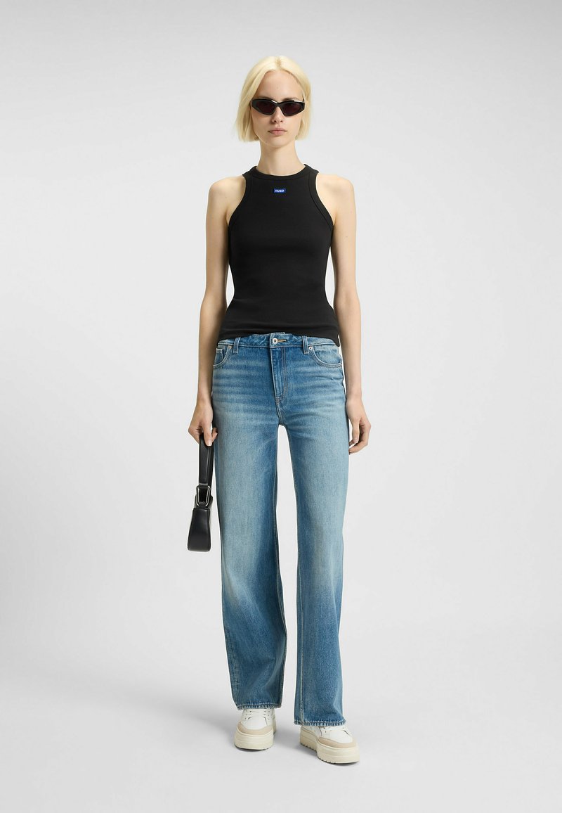 Top senza maniche nero, jeans a gamba larga blu chiaro, sneaker platee bianche e una piccola borsa nera. Tessuto morbido e vestibilità casual.