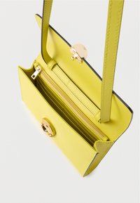 Żółta skórzana torebka o ustrukturyzowanym kształcie, wyposażona w złoty zamek, kieszeń na zamek błyskawiczny oraz wewnętrzne przegródki na karty. Detale obejmują kontrastowe przeszycia.