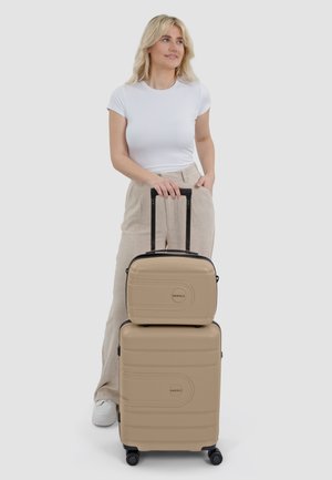 Beige hard-shell koffer set met zwarte accenten, met een gladde textuur, inline wielen en een handvat bovenaan voor gemakkelijke verplaatsing.