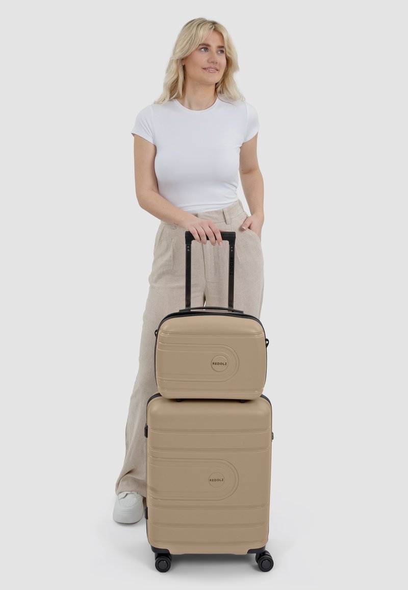 Beige hard-shell koffer set met zwarte accenten, met een gladde textuur, inline wielen en een handvat bovenaan voor gemakkelijke verplaatsing.