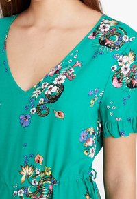 Grünes Blumenkleid mit V-Ausschnitt, kurzen Rüschensäumen und lebhaften, mehrfarbigen botanischen Mustern auf dem gesamten Stoff.