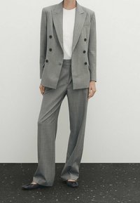 Blazer doppio petto a quadri grigi con bottoni neri abbinato a pantaloni larghi coordinati e una t-shirt bianca, indossato con ballerine blu navy.