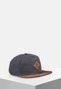 Casquette snapback grise avec un corps texturé et une visière tressée marron, ornée d'un patch en cuir en forme de diamant à l'avant.