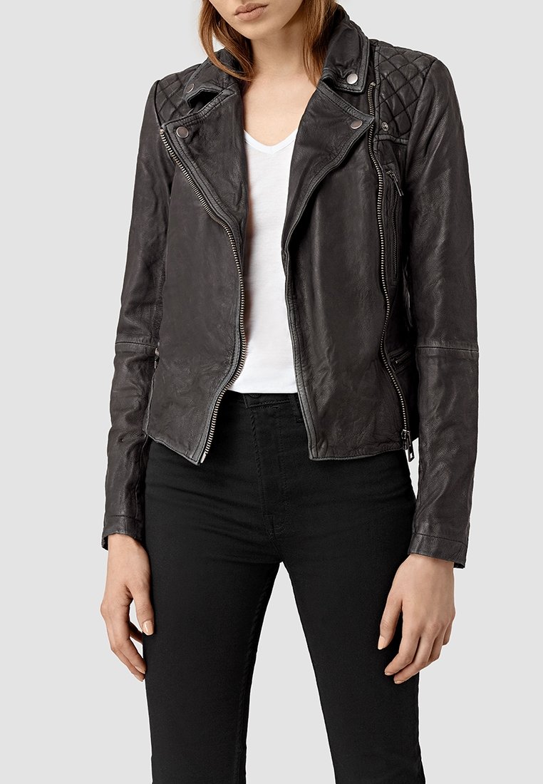 Giacca da motociclista in pelle nera con accenti trapuntati sulle spalle, chiusura con zip asimmetrica e design aderente. Indossata sopra una t-shirt bianca.