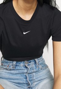 Svart kortärmad T-shirt i bomull med rund halsringning och en vit broderad Nike-logotyp på bröstet. Bärs med högmidjade denimshorts.