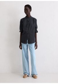 Czarna koszula na guziki z kołnierzem typu band, z podwiniętymi rękawami, w połączeniu z jasnoniebieskimi szerokimi spodniami jeansowymi i beżowymi trampkami. Prosty, nowoczesny design.