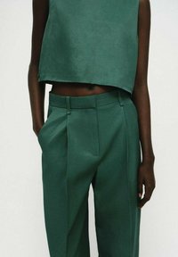 Grüner, kurzer Oberteil und passende, hochgeschnittene Hose. Der Stoff wirkt glatt mit minimaler Textur und weist eine schlanke Silhouette auf.