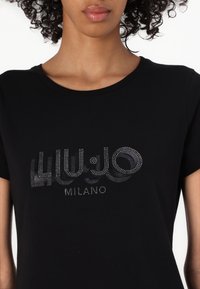 Czarna bawełniana koszulka z krótkim rękawem, z błyszczącym srebrnym logo i napisem "MILANO" z przodu. Okrągły dekolt.