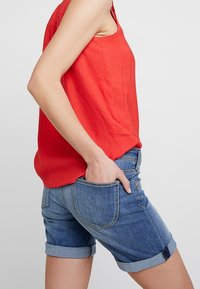 Red sleeveless top made of lightweight fabric paired with rolled cuff denim shorts. The shorts feature back pockets and a relaxed fit.