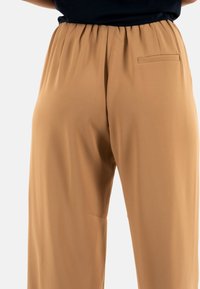 Pantalons larges beiges avec une texture douce, dotés d'une taille élastique et d'un petit détail de poche latérale.